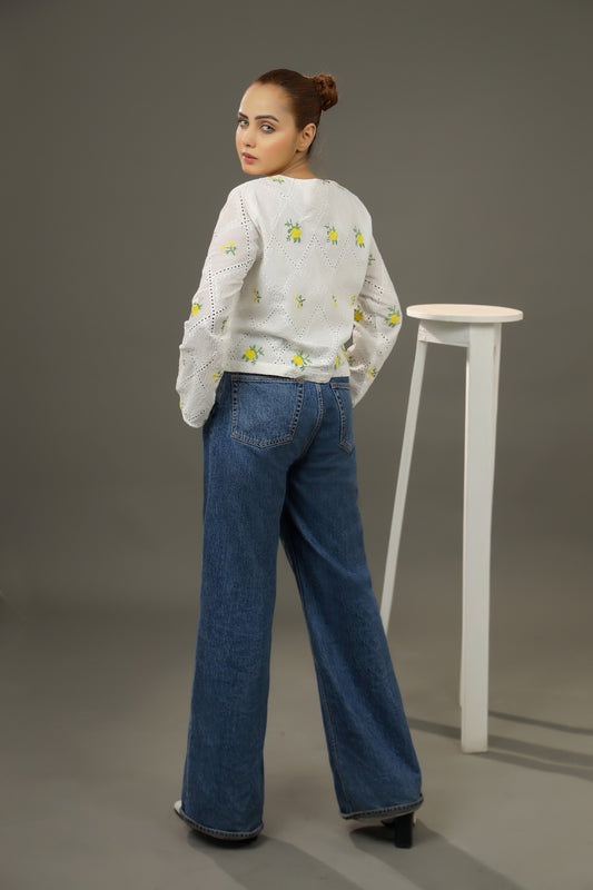 Woman wearing a white embroidered sweater and blue jeans standing against a gray background.Cropped yellow embroidered cardigan-Relaxed body fit-Round neck-Inside hidden hook closure-full lined body-Long sleeves with lace -Fabric: 100% Cotton-backside