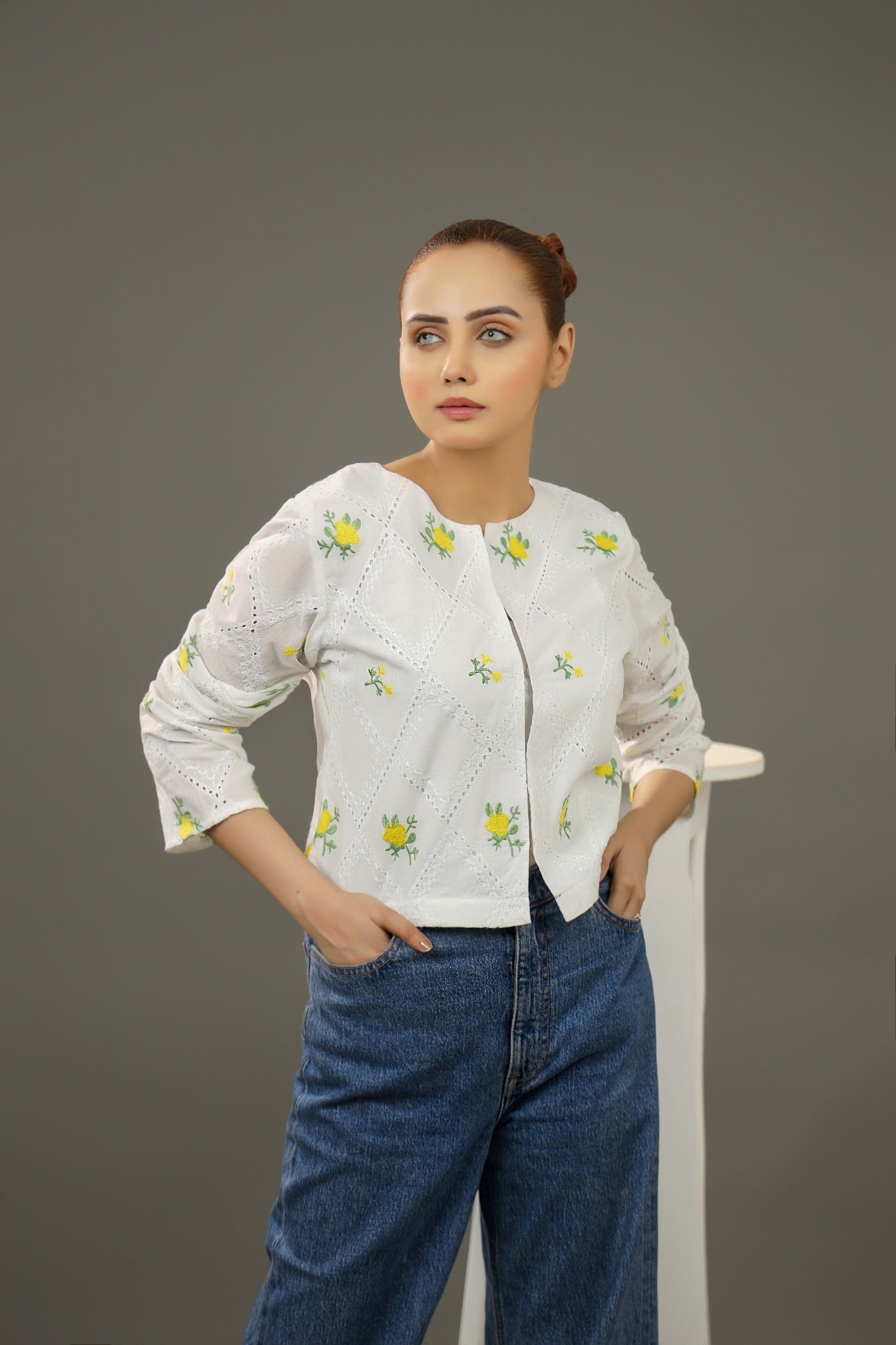 Woman wearing a white embroidered blouse and blue jeans against a gray background.Cropped yellow embroidered cardigan-Relaxed body fit-Round neck-Inside hidden hook closure-full lined body-Long sleeves with lace -Fabric: 100% Cotton-front-closeup
