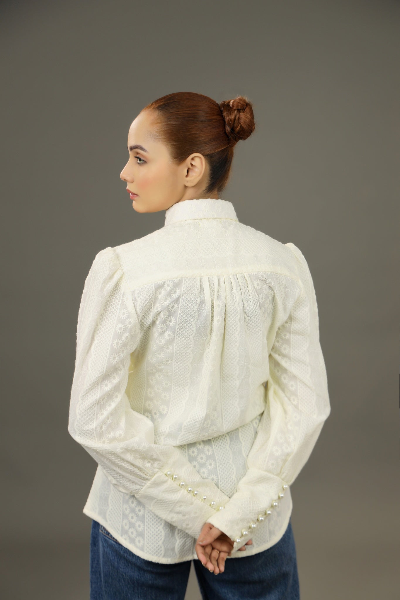 Woman wearing a white embroidered blouse against a gray background.-Embroidered summer-women-Shirt-Relaxed body fit-Structured collar-Pearl buttons-Unlined-Long balloon sleeve with long cuffs-Fabric: 100% Cotton-backview