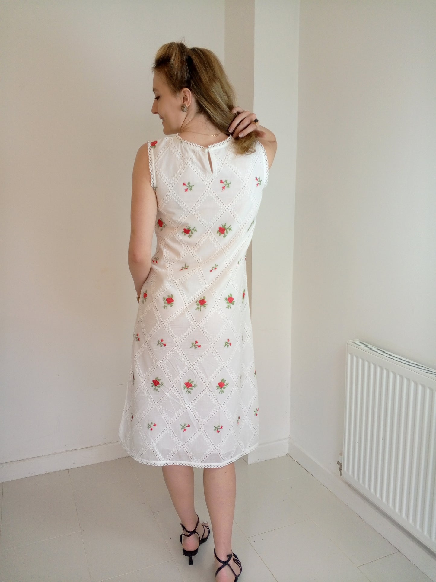 Woman wearing a white dress with floral embroidery in a minimal room.Organic-_cotton-white-summer-woman-dress-red-floral-backside-closeup