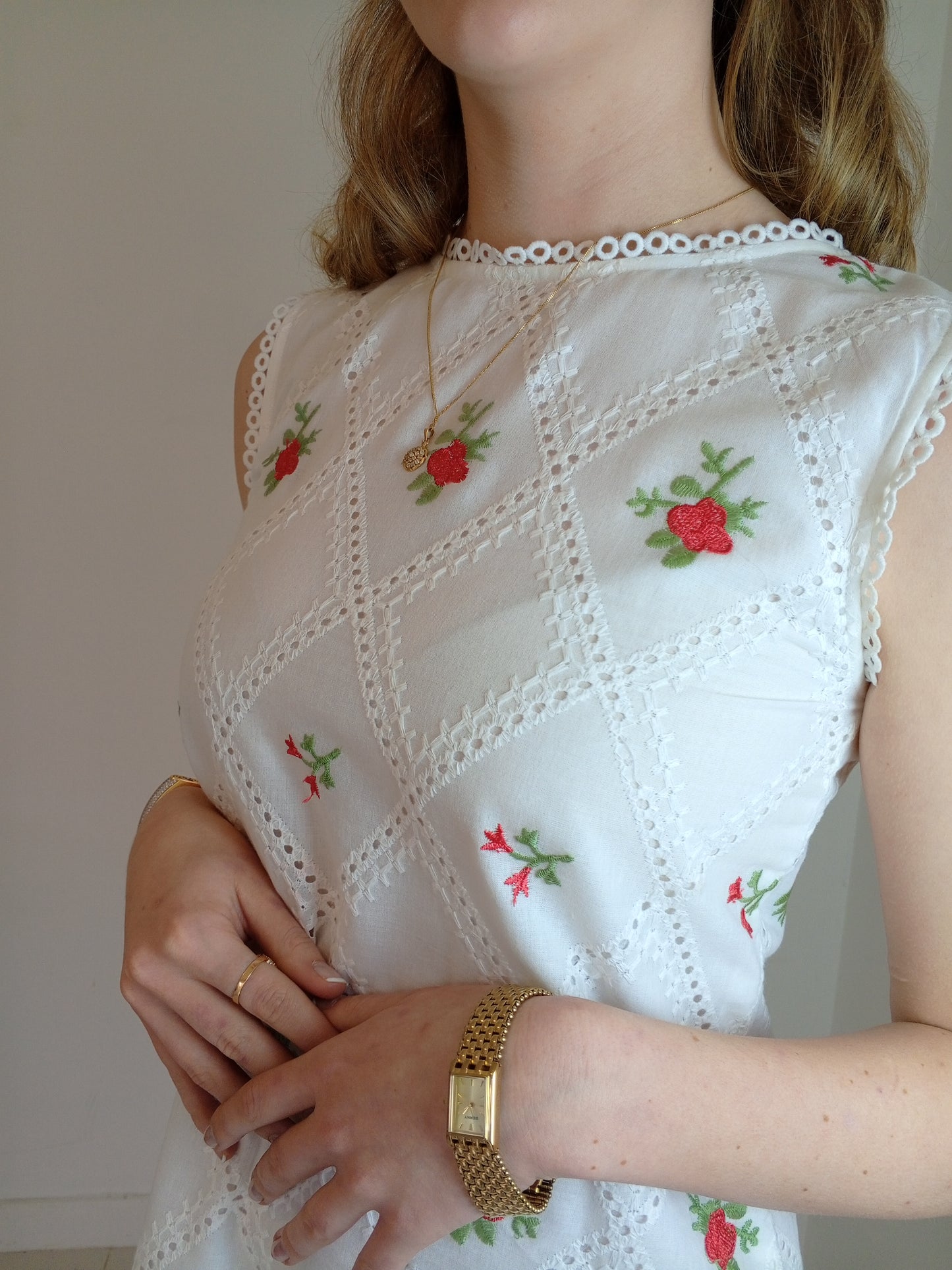 White embroidered top with red floral patterns worn by a person, with a neutral background.Organic-_cotton-white-summer-woman-dress-red-floral-frontside-closeup