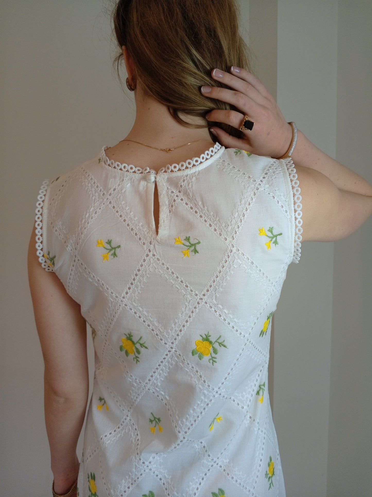 White embroidered dress with yellow floral patterns worn by a person against a plain background