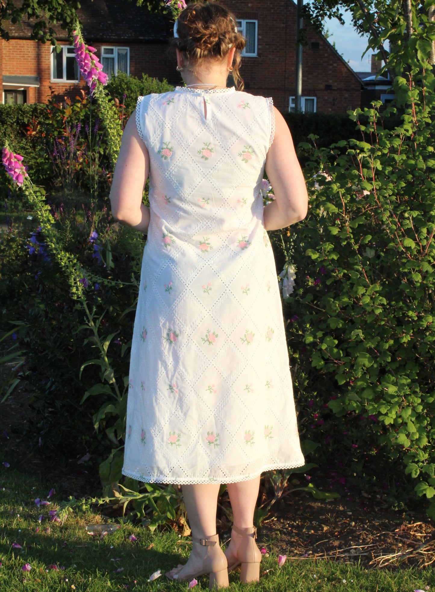 A woman is wearing a Pink and white embroidered dress-Midi length relaxed body fit-Boat neck with lace -left side leg split-full lined dress with soft 100% fine cotton -Sleeveless with lace -Fabric: 100% Cotton-backview