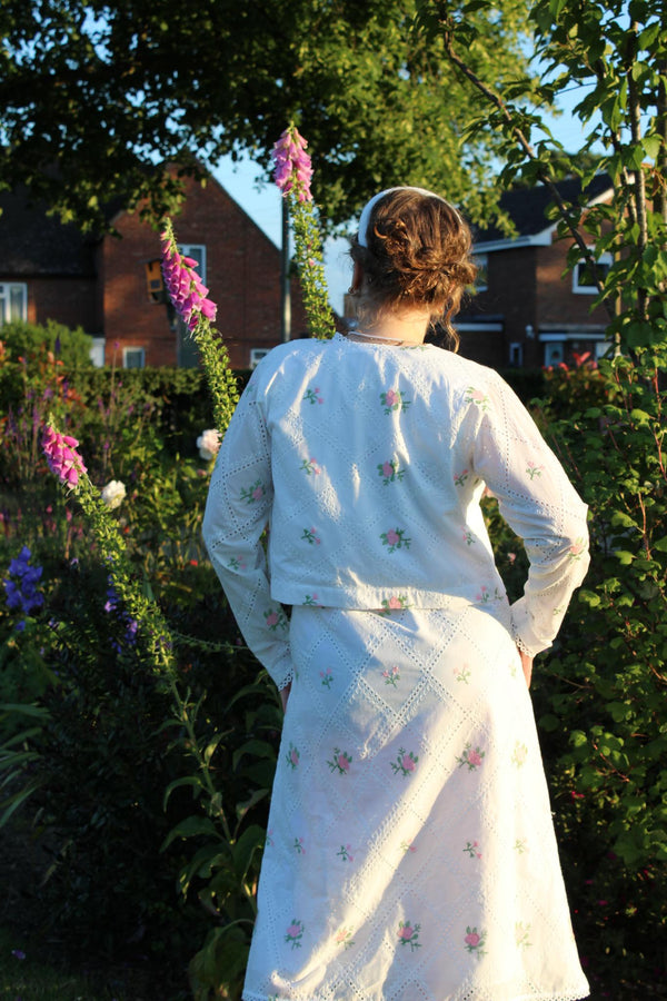 Person wearing a white embroidered Cropped pink embroidered cardigan-Relaxed body fit-Round neck -Inside hidden hook closure-full lined body with100% soft fine cotton-Long sleeves with lace -Fabric: 100% Cotton-backangle