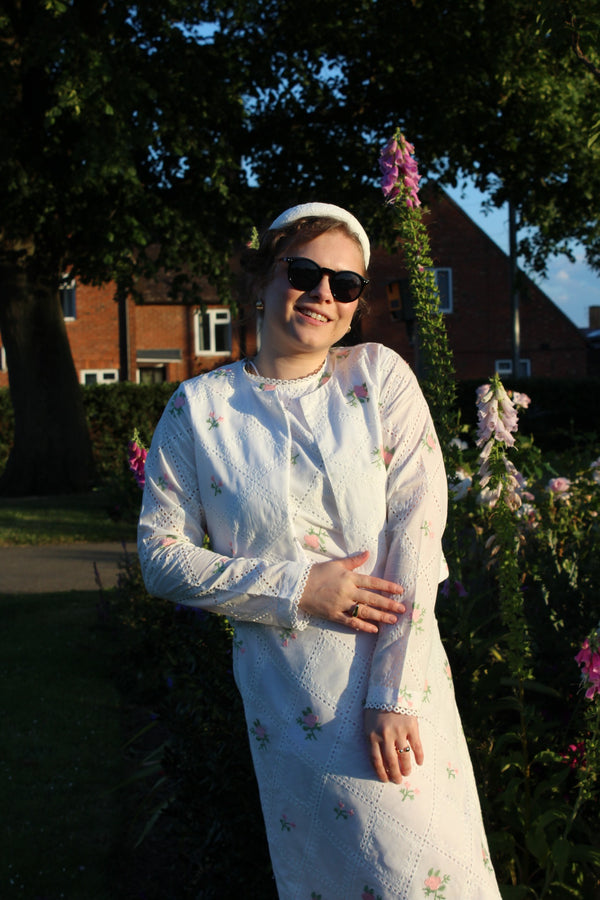 woman in a white dress standing outdoors with flowersCropped pink embroidered cardigan-Relaxed body fit-Round neck -Inside hidden hook closure-full lined body with100% soft fine cotton-Long sleeves with lace -Fabric: 100% Cotton-