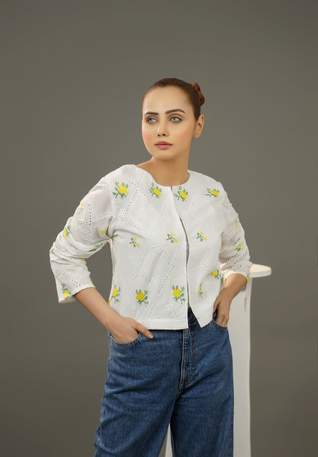 Woman wearing a white embroidered blouse and blue jeans against a gray background.Cropped yellow embroidered cardigan-Relaxed body fit-Round neck-Inside hidden hook closure-full lined body-Long sleeves with lace -Fabric: 100% Cotton-front-closeup