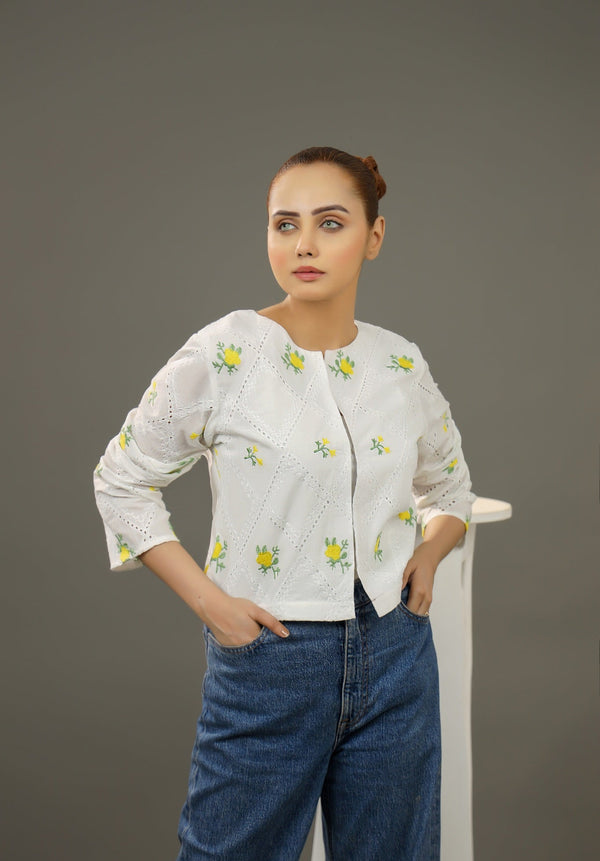 Woman wearing a white embroidered blouse and blue jeans against a gray background.Cropped yellow embroidered cardigan-Relaxed body fit-Round neck-Inside hidden hook closure-full lined body-Long sleeves with lace -Fabric: 100% Cotton-front-closeup