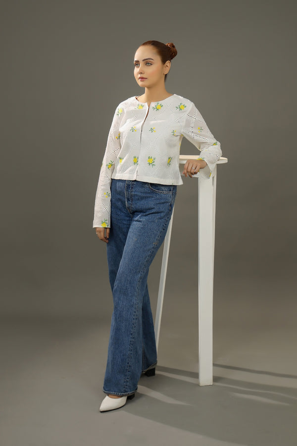 Woman wearing a white embroidered blouse and blue jeans standing against a gray background.Cropped yellow embroidered cardigan-Relaxed body fit-Round neck-Inside hidden hook closure-full lined body-Long sleeves with lace -Fabric: 100% Cotton-sideangle
