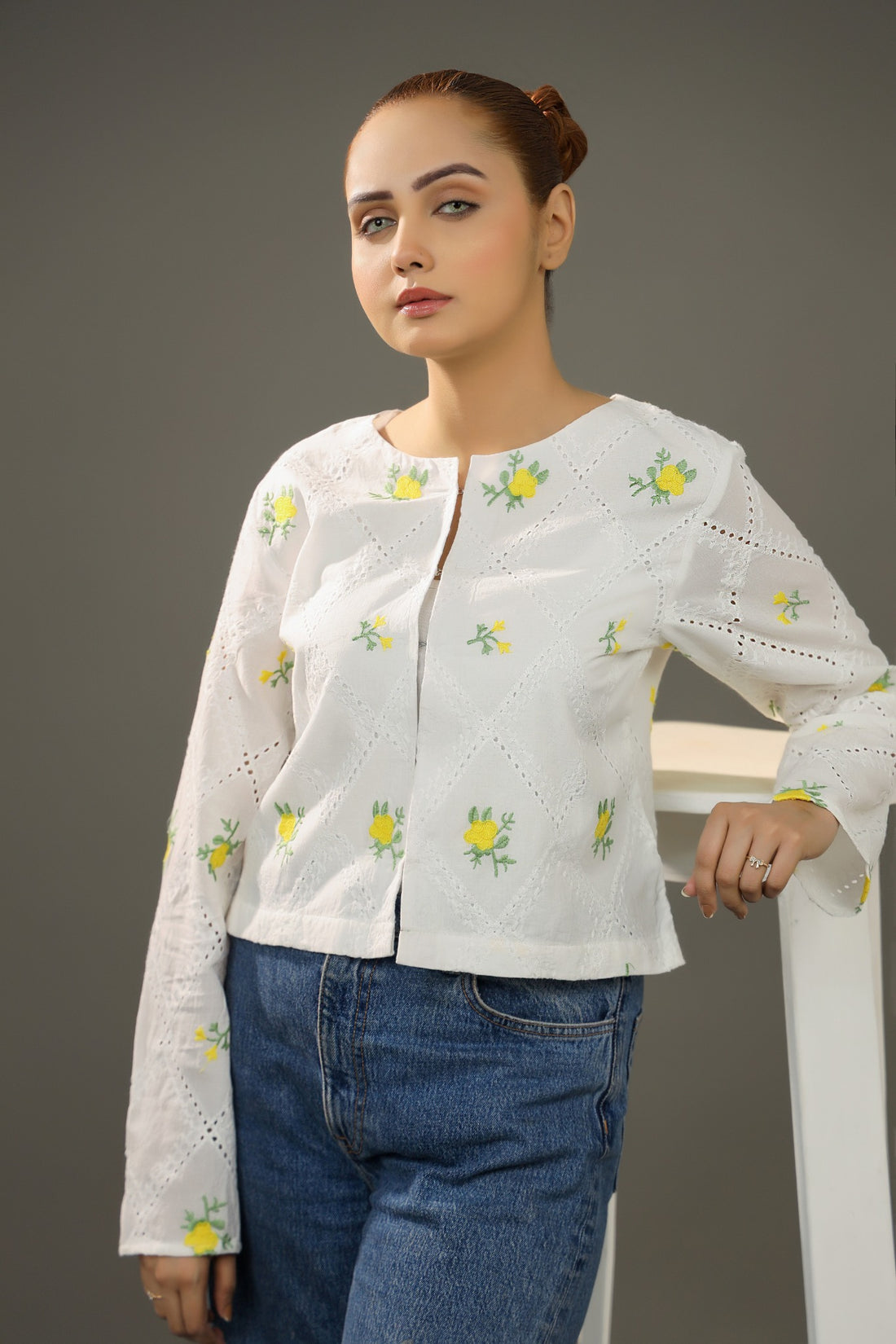 Woman wearing a white embroidered blouse and blue jeans against a gray background.Cropped yellow embroidered cardigan-Relaxed body fit-Round neck-Inside hidden hook closure-full lined body-Long sleeves with lace -Fabric: 100% Cotton-front-closeup