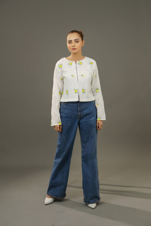 Woman wearing a white embroidered top and blue jeans against a gray background.Cropped yellow embroidered cardigan-Relaxed body fit-Round neck-Inside hidden hook closure-full lined body-Long sleeves with lace -Fabric: 100% Cotton blouse.frontangle