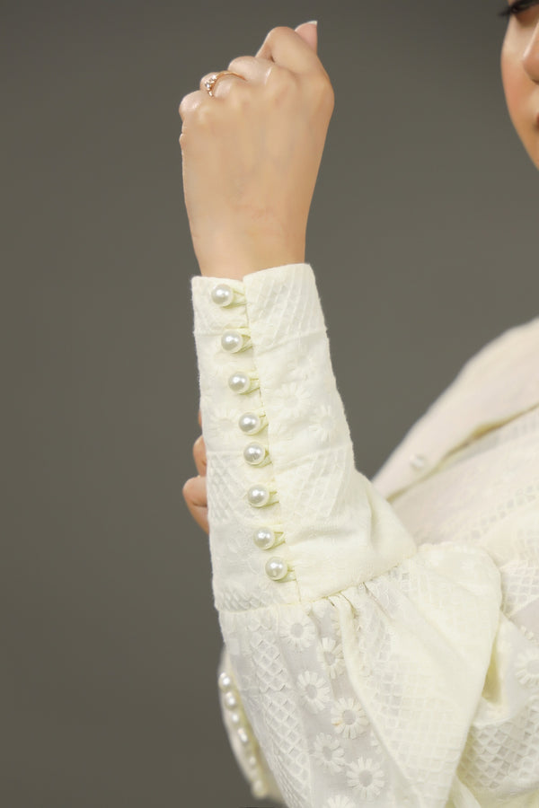 Close-up of a white embroidered garment with pearl buttons on a plain background.-Embroidered  summer-women-Shirt-Relaxed body fit-Structured collar-Pearl buttons-Unlined-Long balloon sleeve with long cuffs-Fabric: 100% Cotton-longcuff-closeup