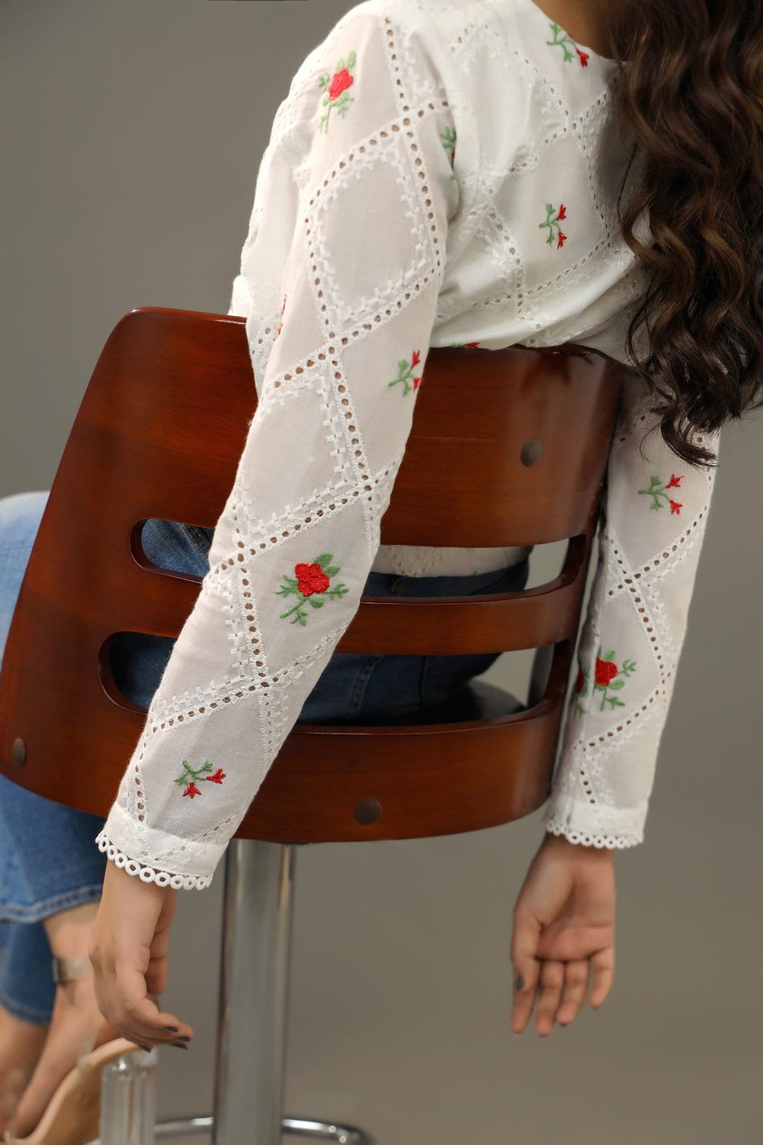 Woman wearing a white embroidered top sitting on a wooden stool against a gray backgroundPremium-organic-cotton-summer-woman-top-floral-red-embroidery