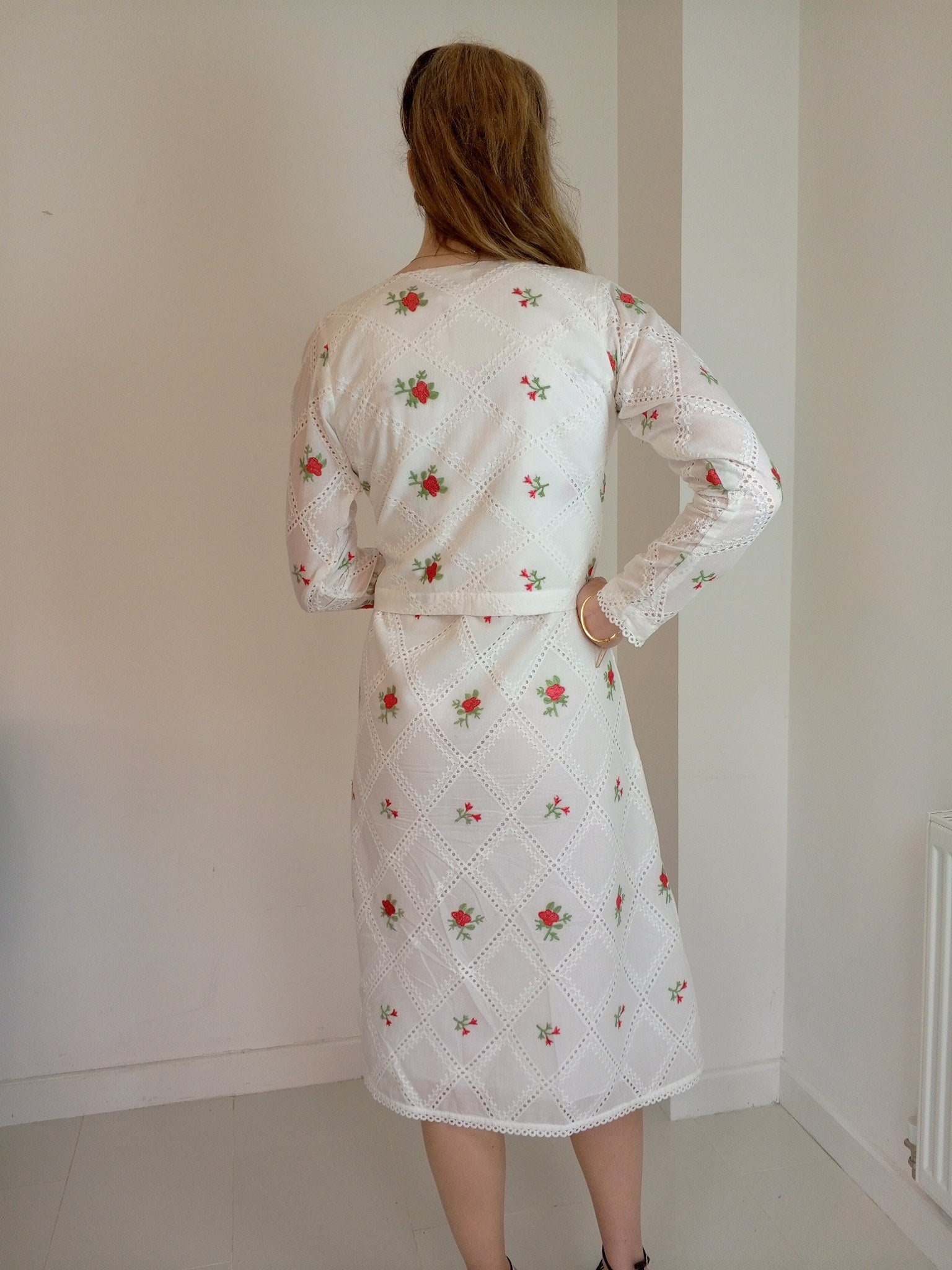 Person wearing a white dress with floral patterns in a minimal indoor Premium-organic-cotton-summer-woman-top-floral-red-embroidery-fullsleeve-matching  jacket with dress -backside