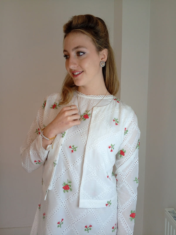 Woman wearing a white embroidered dress with floral patterns indoors.Premium-organic-cotton-summer-woman-top-floral-red-embroidery-fullsleeve-matching  jacket with dress-closeup