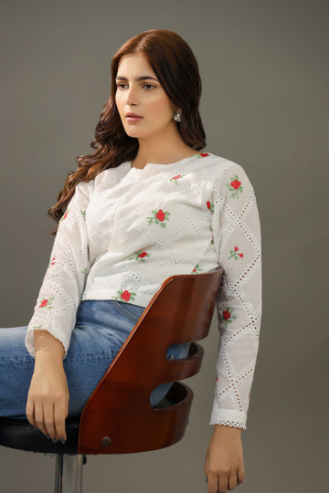 Woman wearing a white embroidered top sitting on a wooden stool against a gray backgroundPremium-organic-cotton-summer-woman-top-floral-red-embroidery